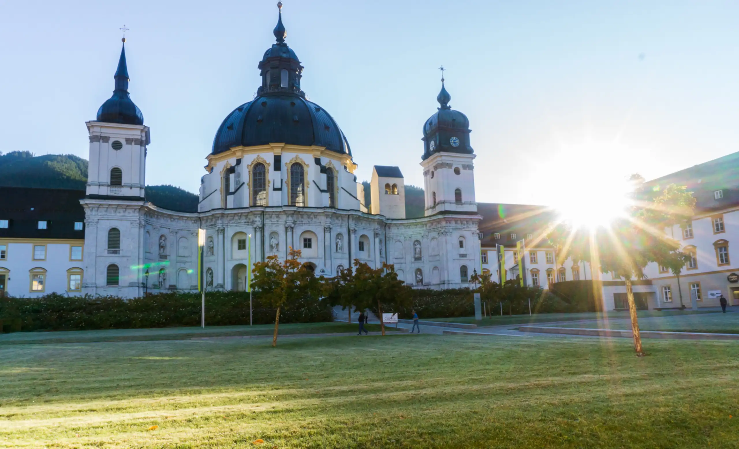 Morgensonne über der beeindruckenden Klosteranlage in Bayern Die Klosteranlage in Bayern erstrahlt in der Morgensonne, umgeben von grüner Wiese und sanften Hügeln, ideal für einen Besuch.