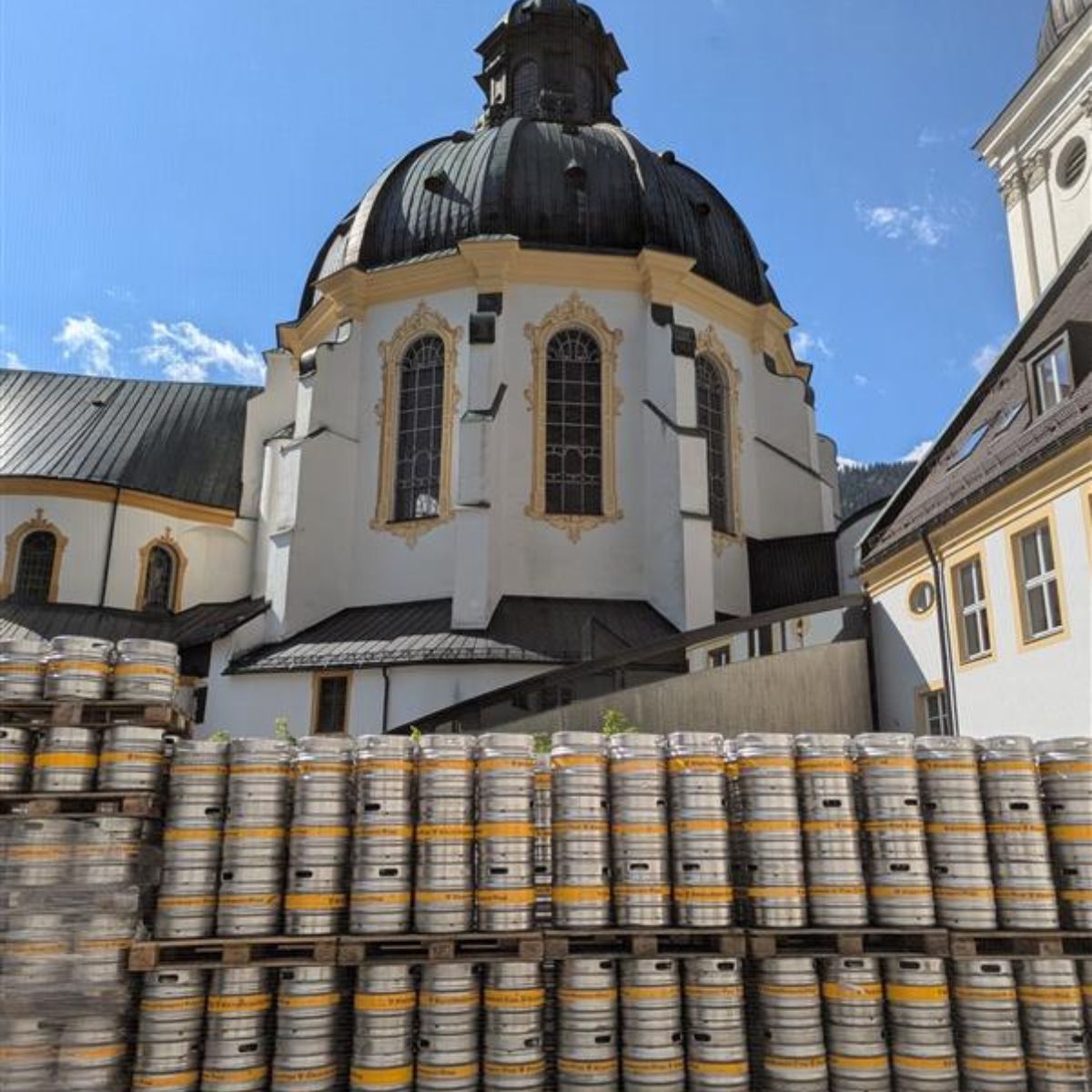 Historisches Kloster mit Bierfässern vor malerischer Kulisse in Bayern Bierfässer vor dem historischen Kloster in Bayern, umgeben von einer beeindruckenden Architektur und blauen Himmel.