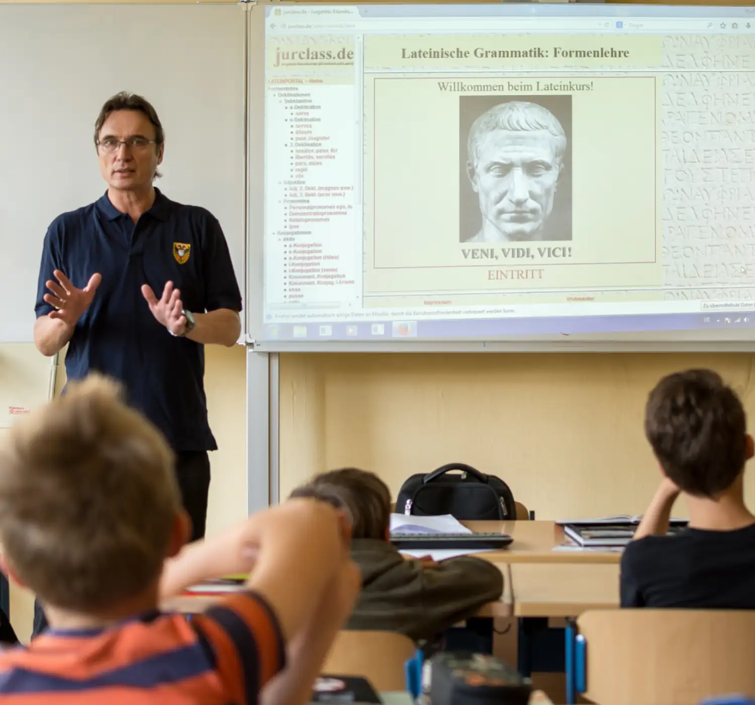 Ein Lehrer erklärt den Lateinunterricht im Klassenzimmer, während Schüler aufmerksam zuhören. Das Thema ist lateinische Grammatik.