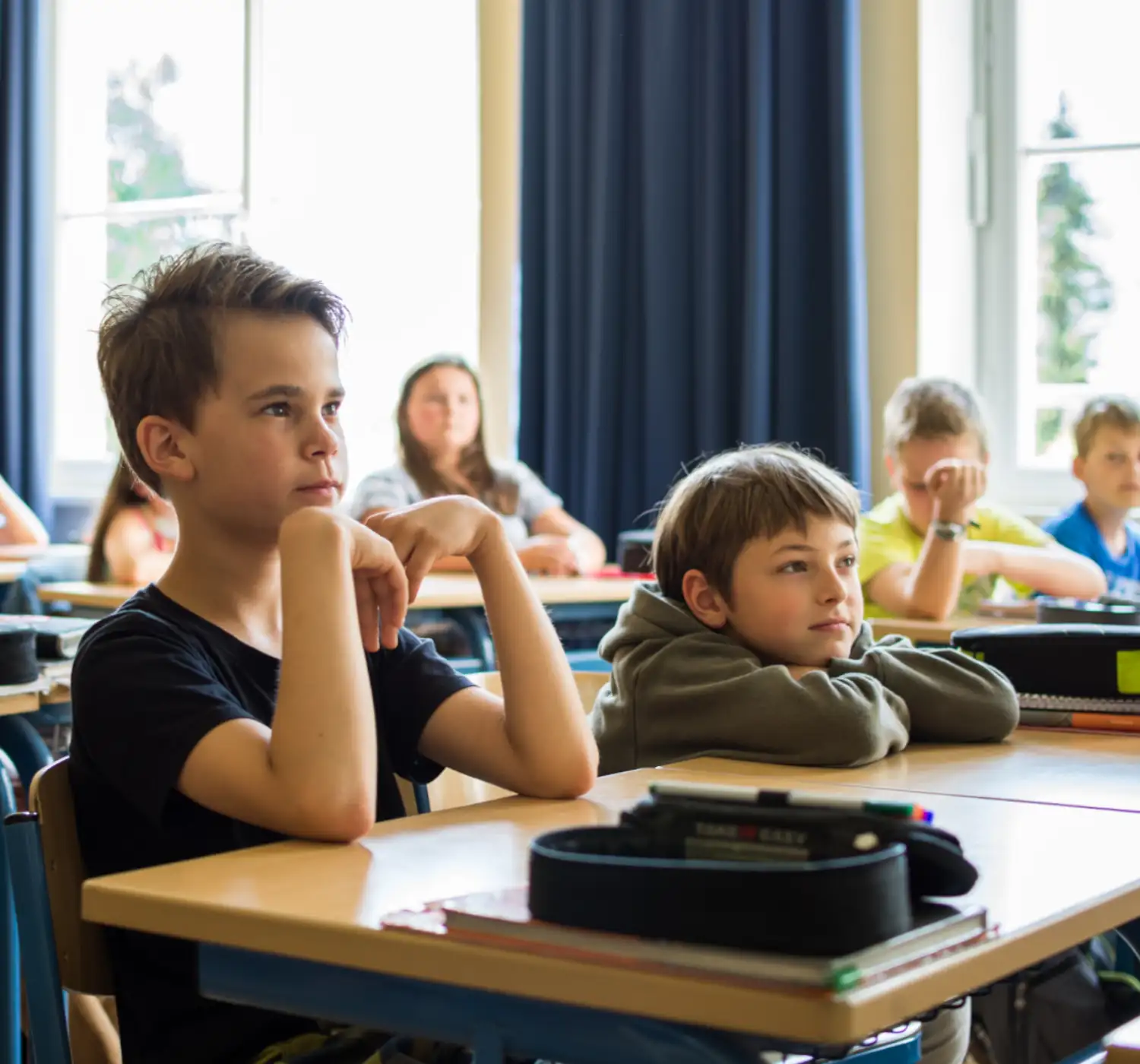 Zwei Schüler im Klassenzimmer lauschen dem Unterricht, während andere Klassenkameraden aufmerksam sitzen.